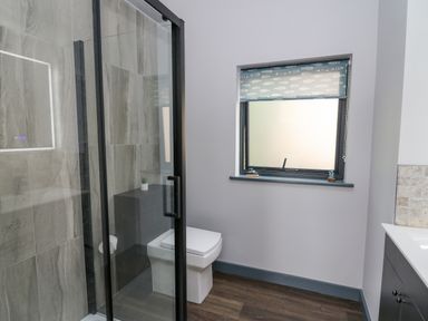 A bathroom with a glass shower enclosure a toilet a window with a patterned blind and a sink unit at Cornerstones Brython in Tenby
