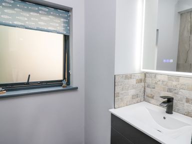 A bathroom sink with a black faucet a lighted mirror and a window with fish patterned blind at Cornerstones Brython in Tenby