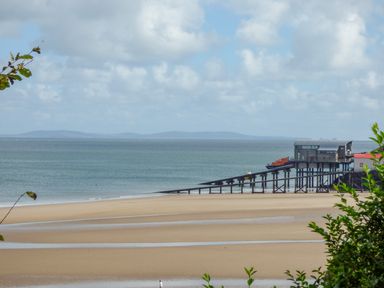 A sandy beach with a long pier extending into the sea and a building on stilts at Cornerstones Brython in Tenby