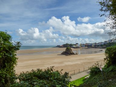 A sandy beach with a rock formation and buildings in the background at Cornerstones Brython in Tenby