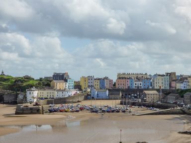 A harbor with boats on sand and colorful buildings behind the harbor at Cornerstones Brython in Tenby