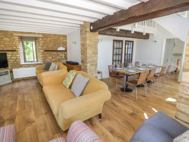 A living room with yellow sofas and a dining table set with plates and glasses at The Paddock in New Yatt near Witney