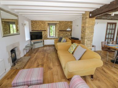 A living room with yellow sofas a striped armchair a television and stone walls at The Paddock in New Yatt near Witney