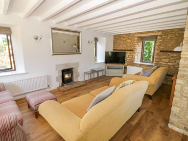 A living room with two yellow sofas a striped armchair a fireplace a wall mirror a television and two windows at The Paddock in New Yatt near Witney