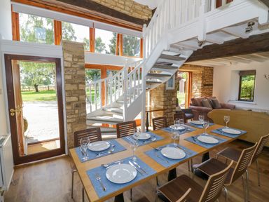 A dining area with a set table and chairs next to a staircase and living room at The Paddock in New Yatt near Witney