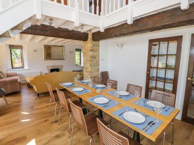A dining area with a set table and chairs near a living room with sofas at The Paddock in New Yatt near Witney