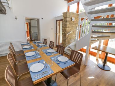 A dining room with a wooden table set for eight next to stairs at The Paddock in New Yatt near Witney