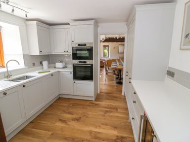 A kitchen with white cabinets a double oven a sink and wooden floor at The Paddock in New Yatt near Witney