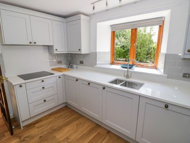 A kitchen with white cabinets a sink window and wooden floor at The Paddock in New Yatt near Witney