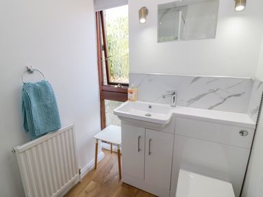 A small bathroom with a white sink cabinet a wooden framed frosted window and a blue towel hanging on a radiator at The Paddock in New Yatt near Witney