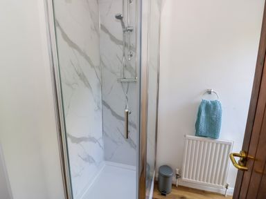 A bathroom with a shower enclosure blue towel on radiator and small trash bin at The Paddock in New Yatt near Witney
