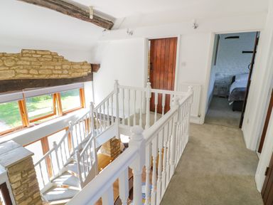 An upper floor hallway with white railings stairs wooden doors and a bedroom doorway at The Paddock in New Yatt near Witney