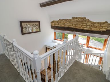A staircase with white wooden railings and a stone wall detail near large windows at The Paddock in New Yatt near Witney