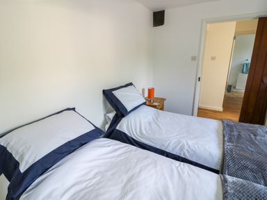 A bedroom with two single beds with white and navy bedding and a wooden nightstand with an orange lamp at The Paddock in New Yatt near Witney