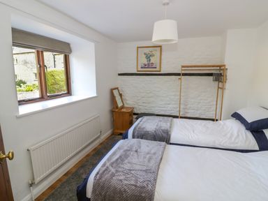 A bedroom with two single beds a wooden nightstand with a mirror a wooden clothes rack and a window at The Paddock in New Yatt near Witney