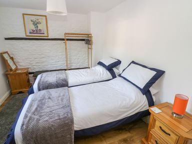 A bedroom with two single beds bedside tables a wooden clothes rack and a framed picture on the wall at The Paddock in New Yatt near Witney