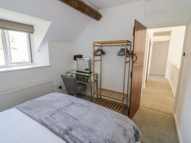 A bedroom with a bed a wooden clothing rack a gray chair and a mirrored desk at The Paddock in New Yatt near Witney
