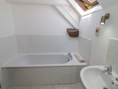 A bathroom with a bathtub a sink a wall light and a skylight window at The Paddock in New Yatt near Witney