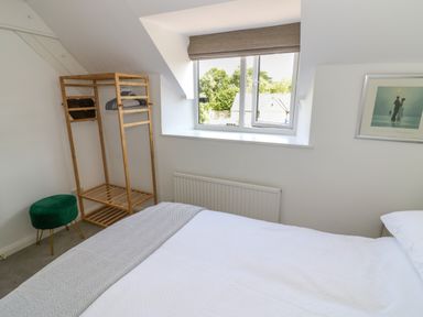 A bedroom with a bed a wooden clothes rack a green stool and a window at The Paddock in New Yatt near Witney