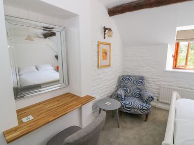 A bedroom corner with a patterned armchair a small round table and a framed picture on a white textured wall at The Paddock in New Yatt near Witney