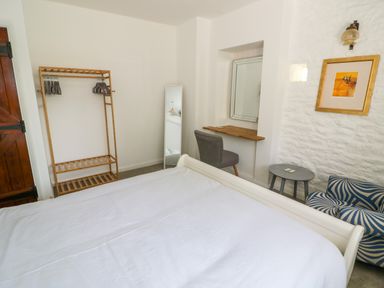A bedroom with a bed white wall wooden clothes rack mirror chair small table and framed picture at The Paddock in New Yatt near Witney