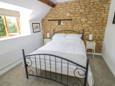 A bedroom with a double bed metal frame white bedding stone wall with wooden beam two bedside tables and lamps at The Paddock in New Yatt near Witney