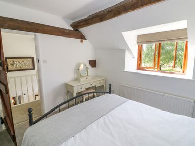 A bedroom with a bed desk mirror window and exposed wood beams at The Paddock in New Yatt near Witney