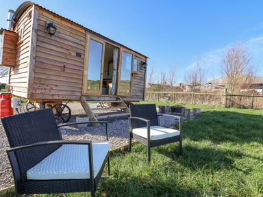 A small wooden caravan with steps and two black chairs with white cushions on grass at Cariad Bach in Gwaenysgor near Prestatyn