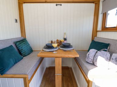 A small dining area with wooden table and cushioned bench seats with pillows at Cariad Bach in Gwaenysgor near Prestatyn