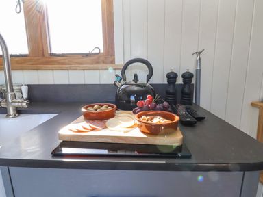 A kitchen counter with a cutting board holding bowls of olives and nuts grapes sliced meat and cheese a black kettle salt and pepper shakers and remote controls at Cariad Bach in Gwaenysgor near Prestatyn