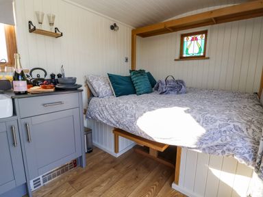 A small room with a bed with pillows and a gray kitchen cabinet with dishes and a champagne bottle at Cariad Bach in Gwaenysgor near Prestatyn