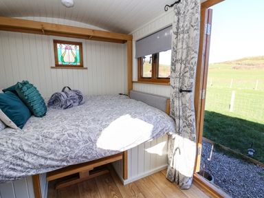 A bedroom with a bed near a window and an open door showing a view of a grassy field at Cariad Bach in Gwaenysgor near Prestatyn