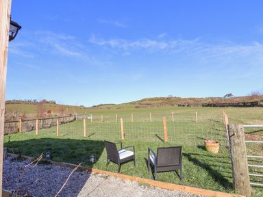 A garden area with two chairs on grass overlooking a fenced field and hills in the distance at Cariad Bach in Gwaenysgor near Prestatyn
