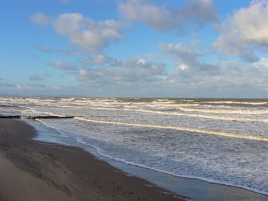 A sandy beach with waves coming ashore under a partly cloudy sky at Cariad Bach in Gwaenysgor near Prestatyn