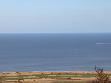 A view of the sea with a boat on the water and grassy land in the foreground at Cariad Bach in Gwaenysgor near Prestatyn