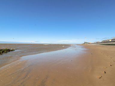 A sandy beach with footprints near water and a sea wall with buildings along the shore at Cariad Bach in Gwaenysgor near Prestatyn