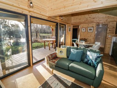 A living room with a green sofa and three cushions opening onto a wooden deck with a table and chairs at Kingfisher in Dunchurch