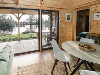 A room with wooden walls round table with white chairs sliding glass door overlooking a patio and pond at Kingfisher in Dunchurch