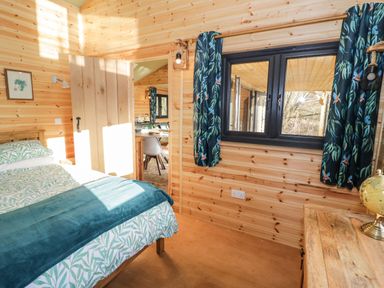 A bedroom with wooden walls a bed a window with patterned curtains and a wooden dresser at Kingfisher in Dunchurch
