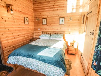 A bedroom with a double bed with patterned bedding and wooden walls at Kingfisher in Dunchurch