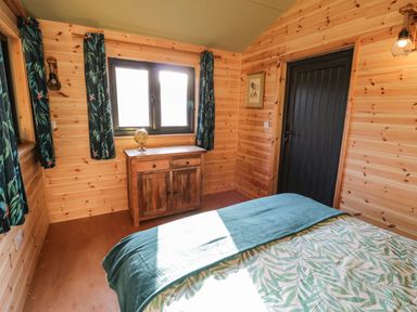 A bedroom with wooden walls a bed a wooden cabinet a globe and curtains at Kingfisher in Dunchurch