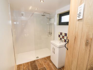 A bathroom with a walk in shower a sink with cabinet a small window and wooden floor at Kingfisher in Dunchurch