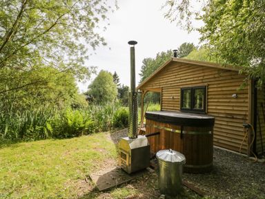 An outdoor area with a wooden hot tub and a metal stove near a wooden cabin at Kingfisher in Dunchurch
