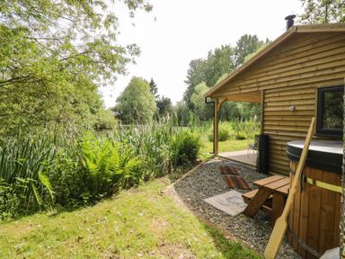 A wooden cabin with a hot tub and paddle next to a grassy area with plants at Kingfisher in Dunchurch