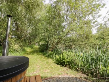 A garden path lined with trees and foliage next to a wooden hot tub at Kingfisher in Dunchurch