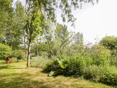 A garden with trees bushes and grass with wooden chairs and a small table at Kingfisher in Dunchurch