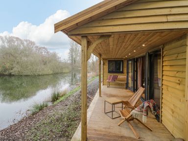 A wooden porch with chairs and a bench by a river at Willow in Dunchurch