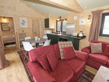 An open living area with red sofas, round dining table with white chairs, kitchen with green cabinets and appliances and wooden walls at Willow in Dunchurch