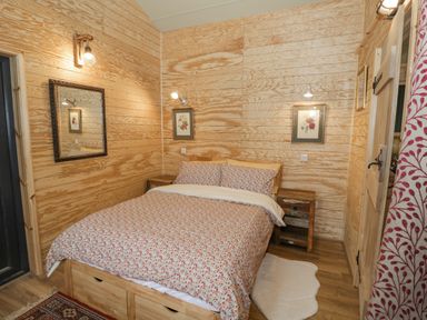 A bedroom with a bed with floral bedding two nightstands and floral pictures on wooden walls at Willow in Dunchurch