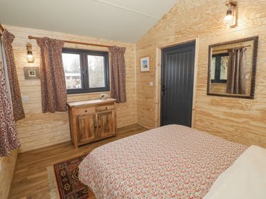A bedroom with a bed a wooden cabinet a window with curtains a mirror on the wall and a door at Willow in Dunchurch